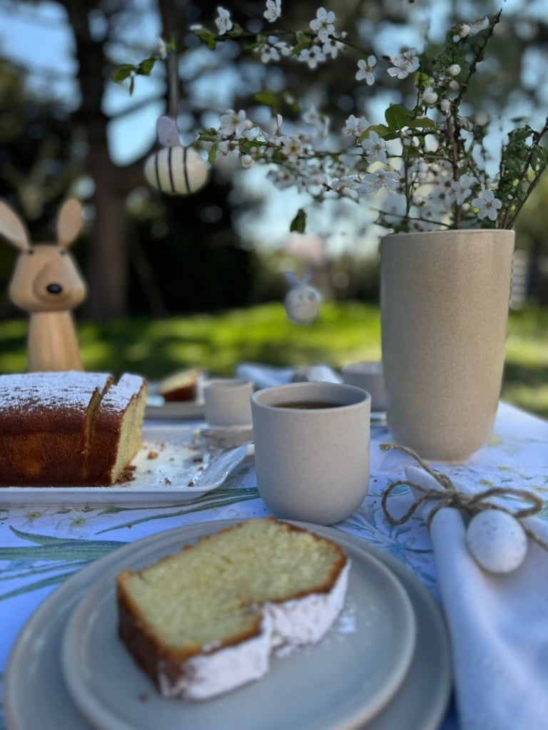 Garden table set up with handmade plates, cups and a lemon cake. Decoration for Easter.